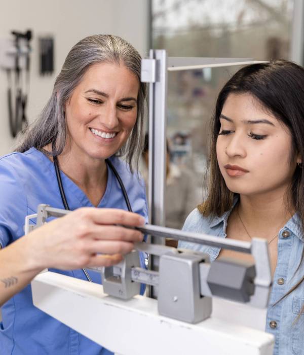 The mature adult female nurse smiles as she see the teenage girl's height and weight.